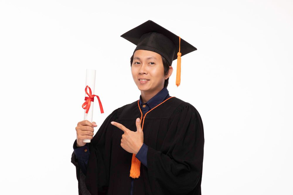 Portrait of smiling man wearing graduation gown against white background-Study in Finland Concept.